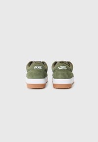 Zapatillas de ante verde con suelas de goma blanca y color caramelo. Cuentan con un collarín acolchado, un forro de patrón en blanco y negro, y el logo de Vans en el talón.