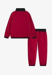 Rote Sportjacke und Hose mit schwarzen Akzenten, elastischen Bündchen und Stehkragen, gefertigt aus glattem, leichtem Material.