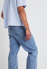 Chemise à manches courtes bleu clair associée à un jean en denim délavé. Le jean présente un design classique à cinq poches avec des détails de coutures visibles.