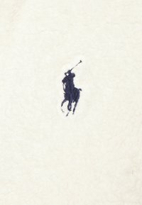 Vitt fleece tyg med en marinblå broderad polo spelarlogotyp. Mjuk textur med en mysig framtoning och utan ytterligare mönster.