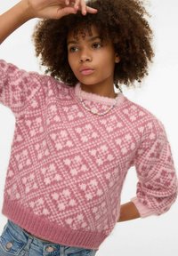 Rozā adīts džemperis ar strukturētu dimanta rakstu, ar īsām piedurknēm un ribotām aprocēm. Modelis valkā krāsainu krelles kaklarotu.