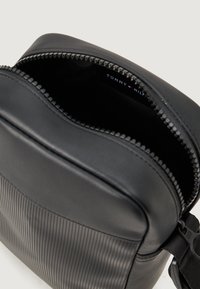 Černá kožená taška přes rameno se zipovým otvorem, na jedné straně s vroubkovanou texturou a na druhé straně se hladkým povrchem. Uvnitř štítek.