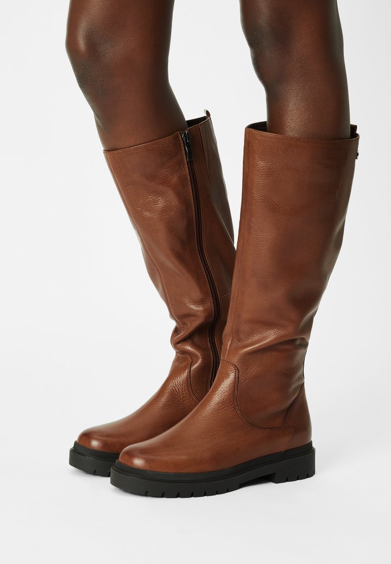 Bottes en cuir marron jusqu'aux genoux avec un fini texturé, dotées d'une fermeture éclair sur le côté et d'une semelle en caoutchouc noir robuste pour une meilleure adhérence.