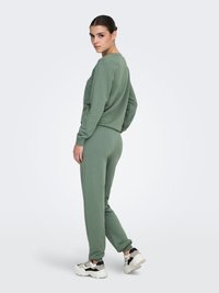 Ensemble sweat-shirt et pantalon de jogging en coton vert, avec une coupe décontractée, des poignets côtelés, et assorti à des baskets blanches et noires épaisses.