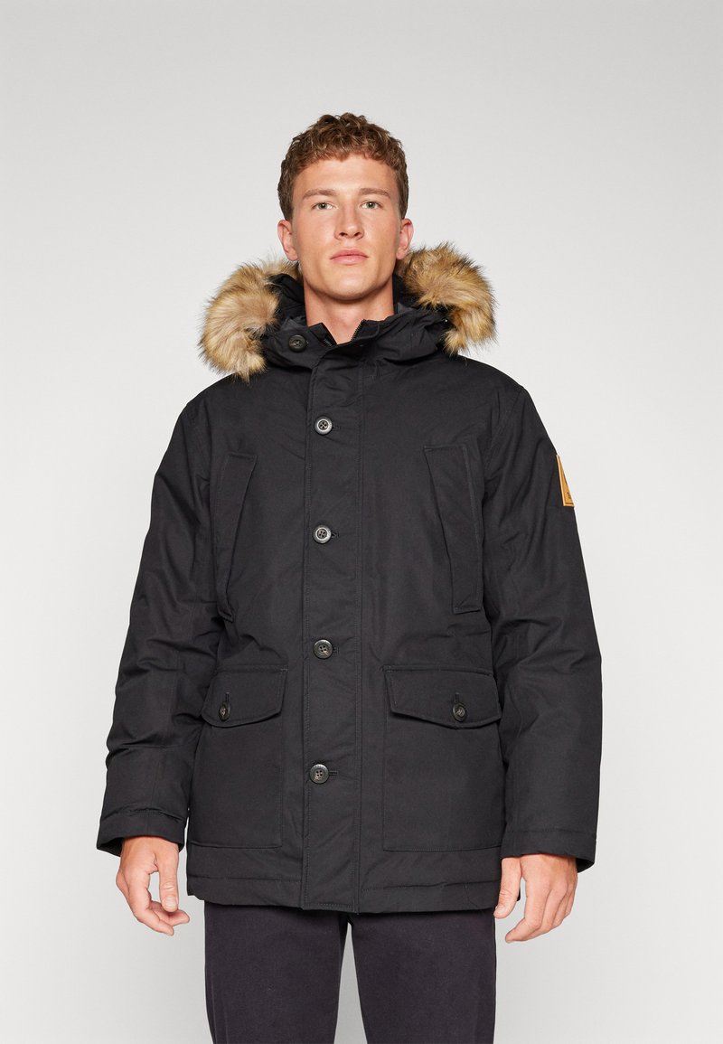 Parka noire avec une capuche en fausse fourrure, des boutons à l'avant, deux grandes poches avant et un design de couture horizontale sur le devant.