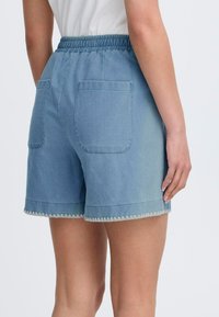 Shorts de mezclilla en azul claro con una textura suave, cinturilla elástica y dos bolsillos en la parte posterior. Presenta un detalle de dobladillo festoneado.