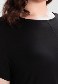 Czarna bluzka z krótkim rękawem, z okrągłym dekoltem i gładką teksturą materiału, z detalami bezszwowymi z przodu.