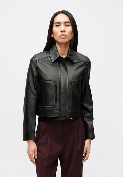 Zwarte leren cropped jas met een spitse kraag, open voorkant, twee grote zakken en gestructureerde schouders, gecombineerd met donkere broek.