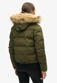 Olijfgroene pufferjack met een capuchon van bont, geribbelde manchetten en een aansluitende tailleband. Bevat een gewatteerd design en zijzakken.