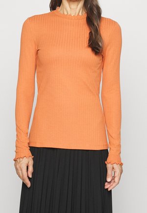 Haut à manches longues en rib avec un col et des poignets volantés, de couleur orange, fabriqué en tissu doux, associé à une jupe plissée noire.