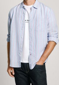 Raitapaitajakku vaaleansinisessä värissä, punaisilla ja valkoisilla raidoilla sekä yhdessä rintataskussa; käytetään valkoisen T-paidan ja tummien farkkujen päällä.