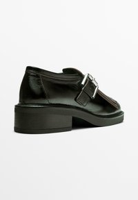 Sort lædersko med en chunky hæl, der har en sidebøjle, flad front og glat tekstur. Designet til et formelt udseende.