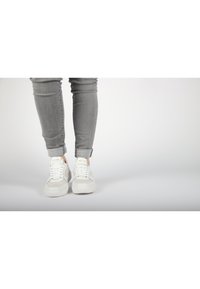 Weiße Sneakers mit einer glatten Leder- und Wildleder-Oberfläche. Schnürsenkel und gepolsterte Zunge. Enganliegende graue Jeans, an den Säumen umgeschlagen.