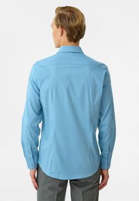 Lichtblauwe overhemd met lange mouwen, gemaakt van een zachte stof, met knoopmanchetten en een gebogen zoom. Eenvoudig ontwerp zonder zichtbare patronen of accenten.