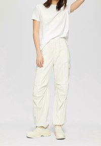 Vit bomullströja i kombination med ljusbeige cargo-byxor som har sidfickor och avslappnad passform, kompletterad med matchande sneakers.