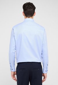 Lichtblauwe shirt met lange mouwen en een puntige kraag, voorzien van knopenmanchetten en een gladde textuur. Draagt met donkere broeken, met een nette achterkant.