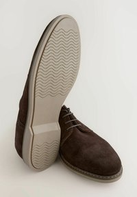 Braune Wildlederschuhe mit abgerundeter Zehe, grauen Schnürsenkeln und einer Gummisohle mit wellenförmigem Profil; glatte Textur mit detaillierten Nähten.
