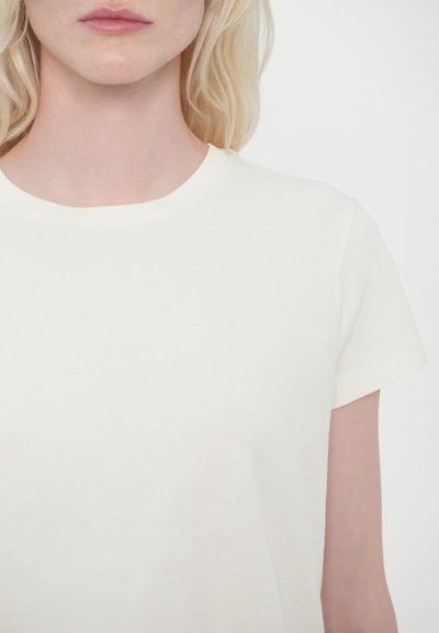 T-shirt à manches courtes et col rond en coton écru, présentant une texture douce et un design minimaliste, sans motifs ni accents visibles.