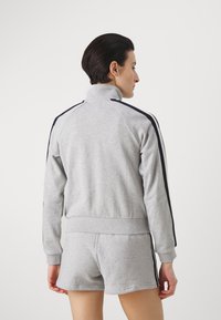 Grå atletisk treningsdress med høy krage. Har marineblå side-striper. Myk tekstur, tettsittende fasong og kort design med elastisk midjebånd.