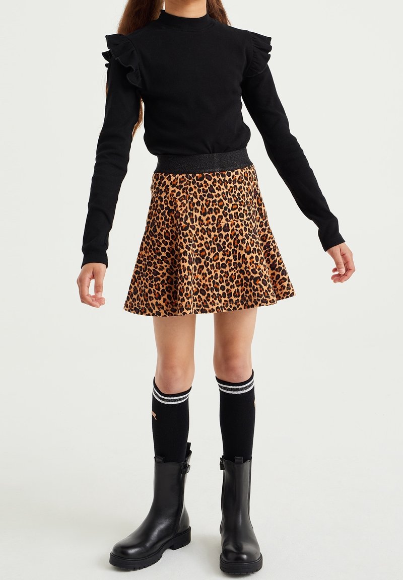 Enfant portant un haut à manches longues noir à volants, une jupe à imprimé léopard, des chaussettes noires montantes avec des rayures blanches, et des bottines noires.