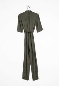 Olivgrüner Jumpsuit mit Kragen, Drei-Viertel-Ärmeln, tailliertem Bund und lässiger Passform, hängt an einem schwarzen Haken.
