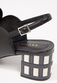 Sandale en cuir noir avec bride à boucle argentée et talon bloc épais avec un motif à carreaux noir et blanc.