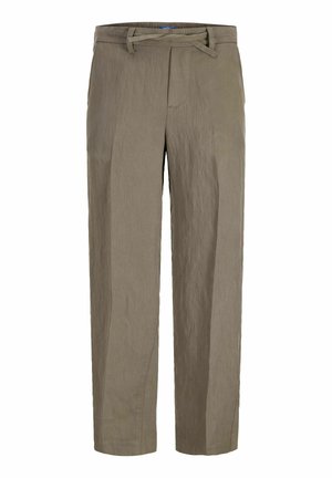 Blond chlapec stojí, nosí svetlozelené polo s krátkym rukávom, voľné béžové nohavice a čierne topánky, pozerá sa doprava.