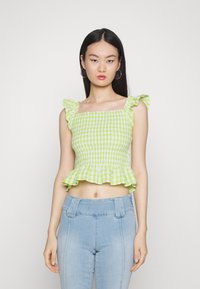 Top cropped de gingham verde com alças franzidas, corpete pregueado e bainha em peplum. Combinado com jeans de cintura alta azul claro.