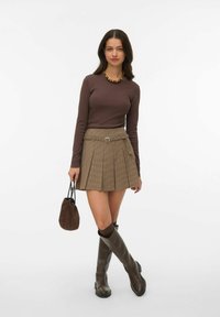 Bruine top met lange mouwen, geruite bruine minirok met riem, kniehoge bruine laarzen en een bruine suède tas. Eenvoudig ontwerp met een gestructureerde afwerking.