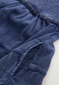 Gros plan d'un tissu texturé bleu marine avec couture froncée et détail de bordure en dentelle sur un vêtement.