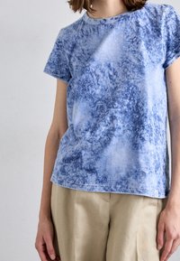 Camiseta de algodón azul con un patrón texturizado de tie-dye. Presenta mangas cortas, escote redondo y un corte relajado. Dobladillo cosido a máquina.
