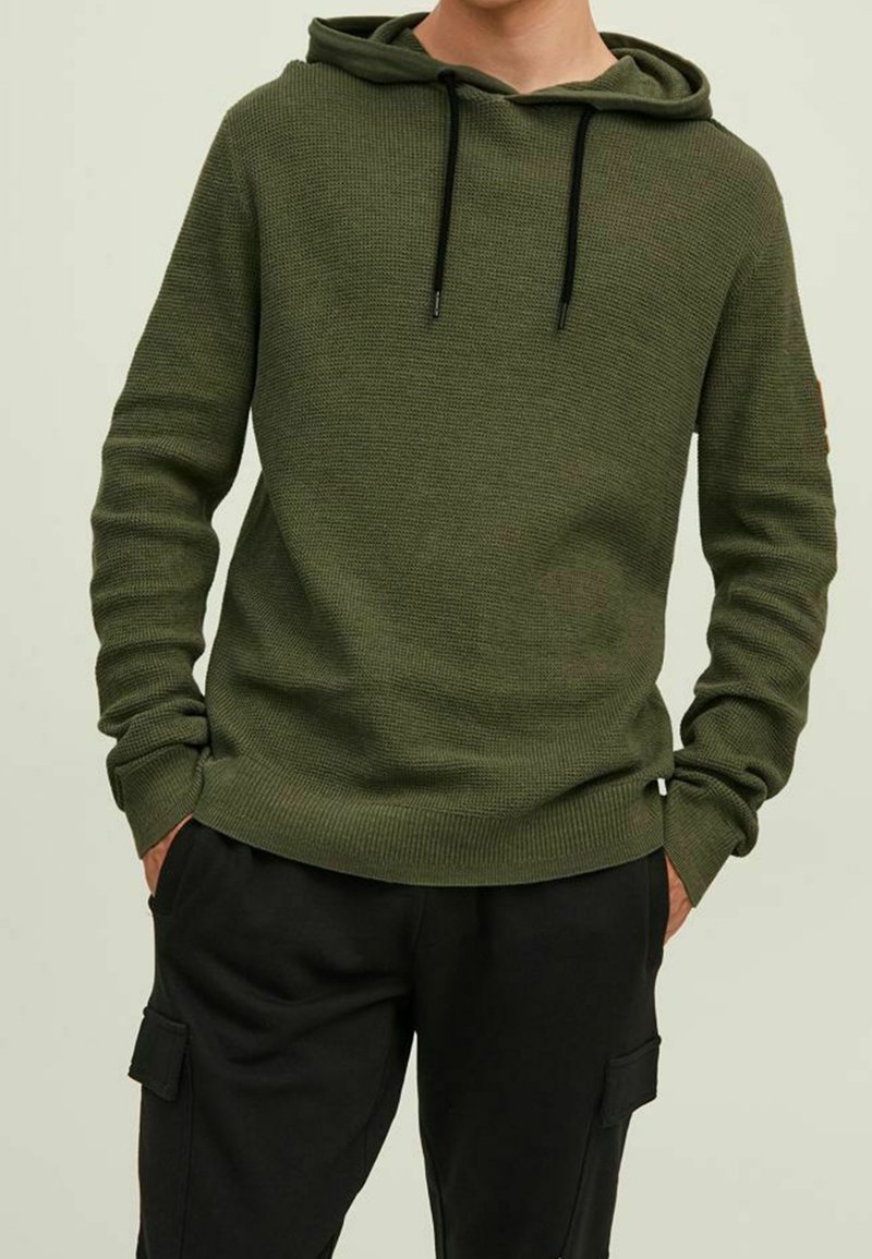 Oliwkowy dzianinowy hoodie z teksturowanym wzorem, z regulowanym kapturem, ściągaczami przy mankietach i u dołu, zestawiony z czarnymi spodniami cargo.