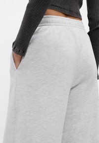 Ανοιχτό γκρι φόρμες με ελαστική μέση και πλαϊνές τσέπες, κατασκευασμένες από μαλακό ύφασμα με λεία υφή.