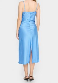 Blå satin midiklänning med justerbara spaghettiaxlar, slits bak, slät textur och lätt lyster. Svarta sandaler med remmar.