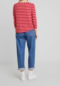 Maglietta a maniche lunghe a righe rosse e rosa con scollatura rotonda, abbinata a jeans azzurri con risvolto e sneaker bianche.