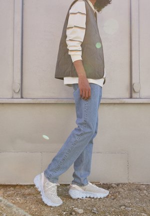 Sneakers bianche trapuntate con tomaia testurizzata e suola screziata. Indossate con jeans azzurri, una camicia a righe bianca e un gilet scuro.