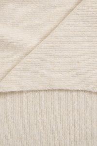 Texturovaná krémová látka s žebrovaným vzorem, která zobrazuje dvě překrývající se vrstvy měkkého, lehkého materiálu.