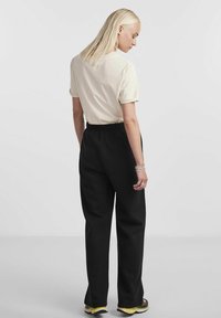 Lys beige bomulls t-skjorte med rullearmer, sammen med svarte bukser med elastisk midje, som viser en avslappet passform. Utsmykket med et sølvarmbånd.