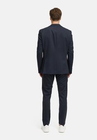 Abito navale su misura con giacca strutturata e pantaloni slim-fit. Tessuto liscio con una sottile trama, abbinato a sneaker bianche.