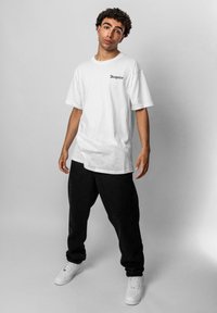 Hvid bomulds T-shirt med korte ærmer og "Dropsize" logo i sort, parret med sorte løstsiddende bukser og hvide sneakers.