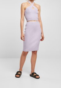 Světle fialový pletený crop top s klíčovou výřezem, v kombinaci s odpovídající sukní ke kolenům, doplněný černými sandály.