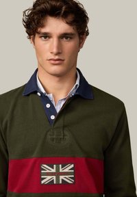 Zielona koszulka do rugby z granatowym kołnierzem, z poziomym czerwonym pasem i naszywką z brytyjską flagą oraz haftem "HACKETT".