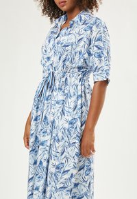 Abito a camicia blu e bianco con motivo floreale, maniche corte, colletto e vita elasticizzata fissata da un cordoncino.