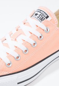 Baskets en toile couleur pêche avec lacets blancs, œillets argentés et semelle en caoutchouc noire. Présentent une étiquette en tissu avec le logo "Converse Star".
