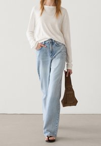 Camicia leggera a maniche lunghe abbinata a jeans a gamba larga azzurri a vita alta. La modella porta una borsa in suede marrone.