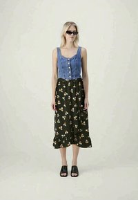 Τζιν τοπ με κουμπιά μπροστά, συνδυασμένο με μια σκούρα πράσινη, midi φούστα με λουλουδάτο σχέδιο και ριχτό στρίφωμα. Το μοντέλο φοράει μαύρα σανδάλια slide.