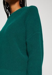 Turkusowy sweter dziany o prążkowanej fakturze, z okrągłym dekoltem i opuszczonymi ramionami. Zaprojektowany dla swobodnego kroju i casualowego stylu.