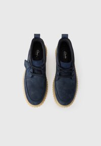 Navy leather shoes feature a rounded toe, flat laces, and a textured beige rubber sole. A loop at the heel aids in easy wear.