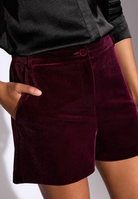 Burgundijas samta šorti ar gludu tekstūru, ar sānu kabatām, pogu aizdari un pieguļošu dizainu. Apvienoti ar melnu satīna topu.