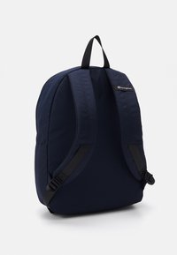 Sac à dos bleu marine fabriqué en tissu résistant, avec des bretelles rembourrées et un petit patch de logo en haut. Design élégant avec une forme minimaliste.